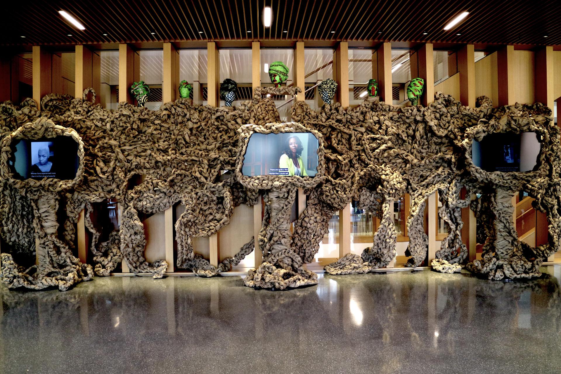 Installation view of STUFF by Dianne Smith, showing elements including butcher paper, African fabric, wooden mannequin heads, and video screens.