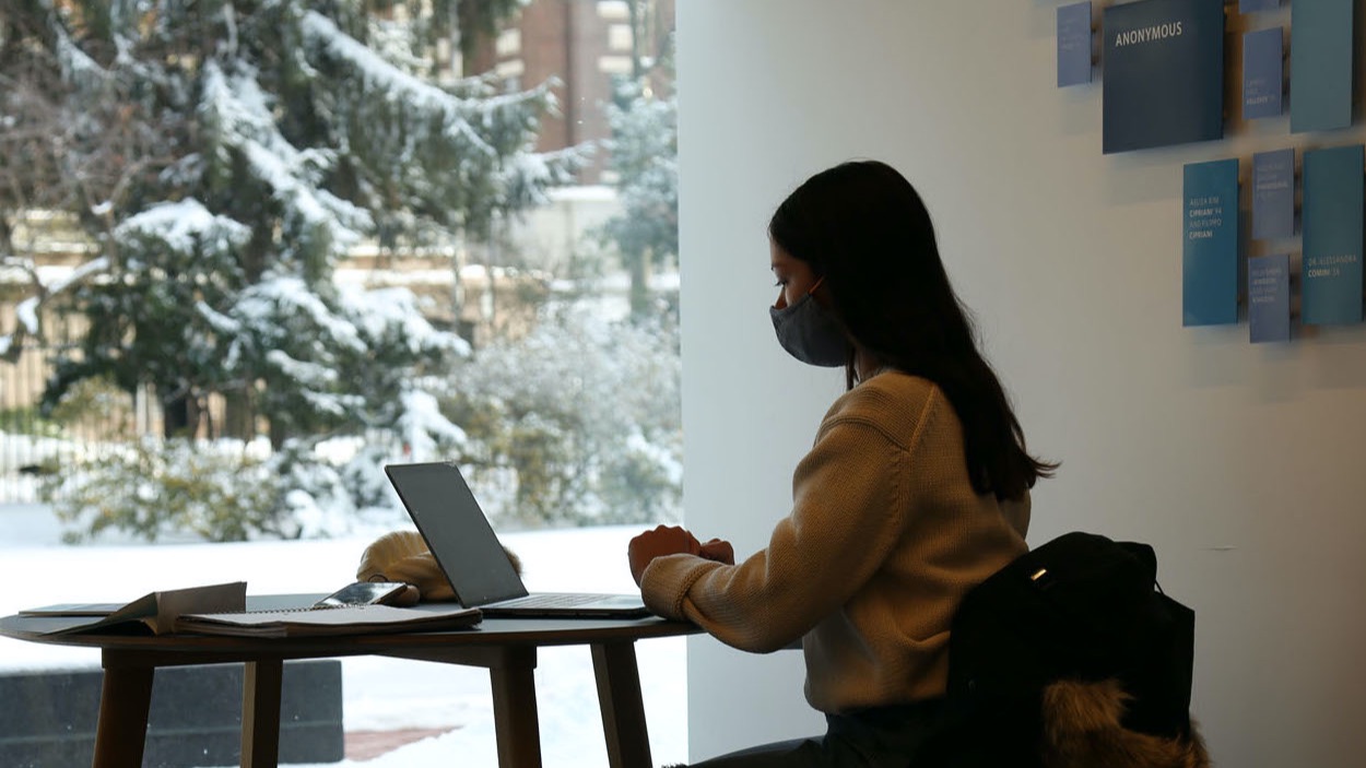 Student wearing a mask and sitting at a desk in Milstein on her laptop.