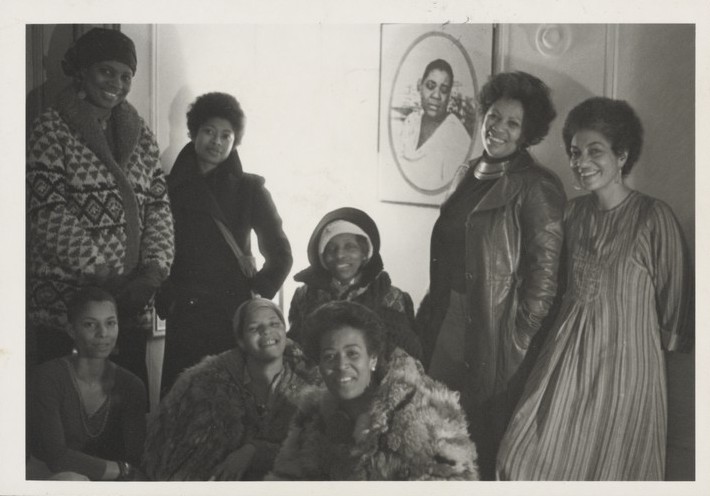 A black & white photo form 1977 of 8 women smiling.