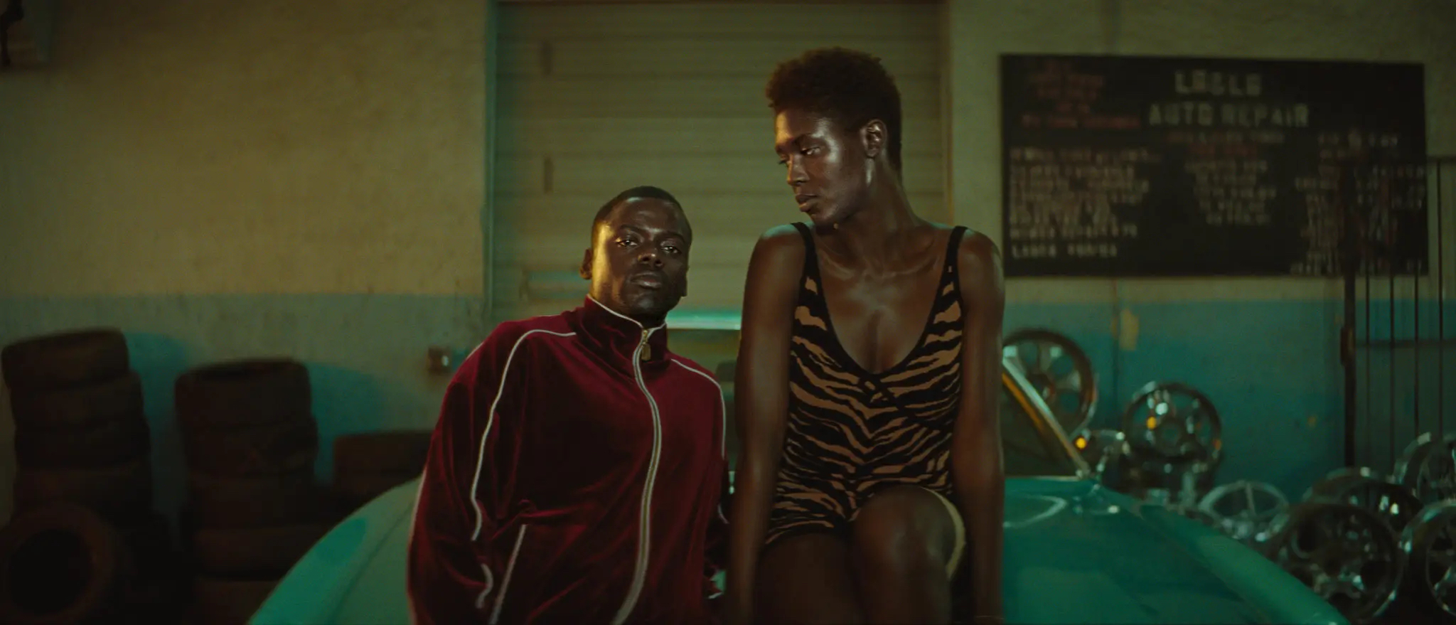 Queen and Slim sitting on the hood of a car. Queen is looking at Slim, and Slim is looking straight ahead.