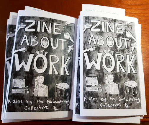 photo of two piles of A Zine About Work: white handwritten title on dark background with drawings of work icons like a computer and a person on the phone