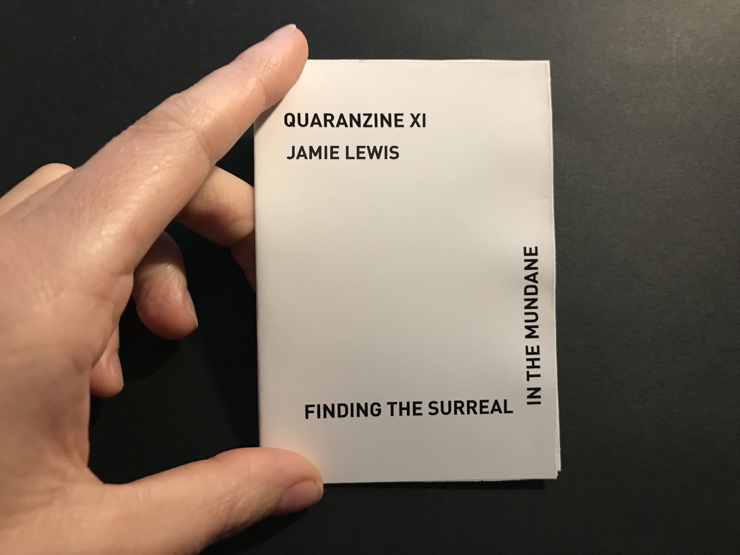 photo of hand holding zine: black text in L shape