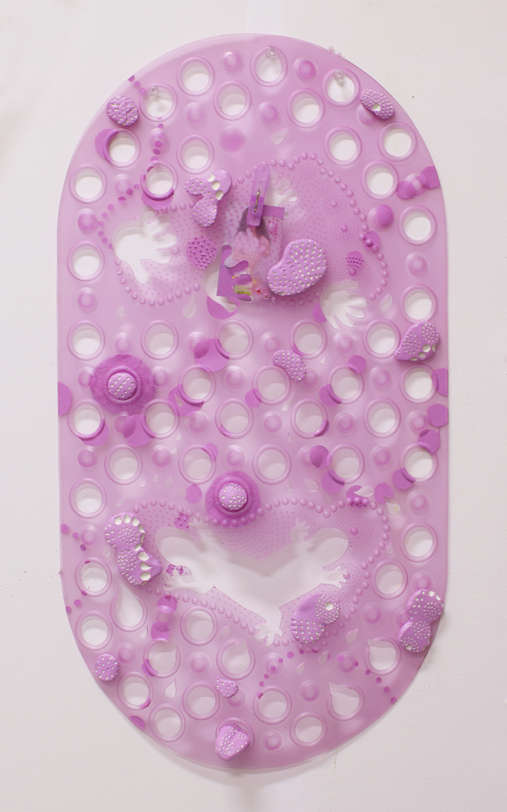 Lavender plastic bath mat hanging on the wall, with hand-like and abstract shapes cut out of it, and blobs of polymer clay painted to match the color of the mat attached to the surface.