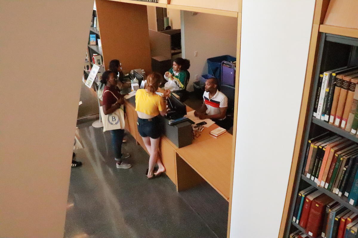 Three students talking with two circulation desk staff.