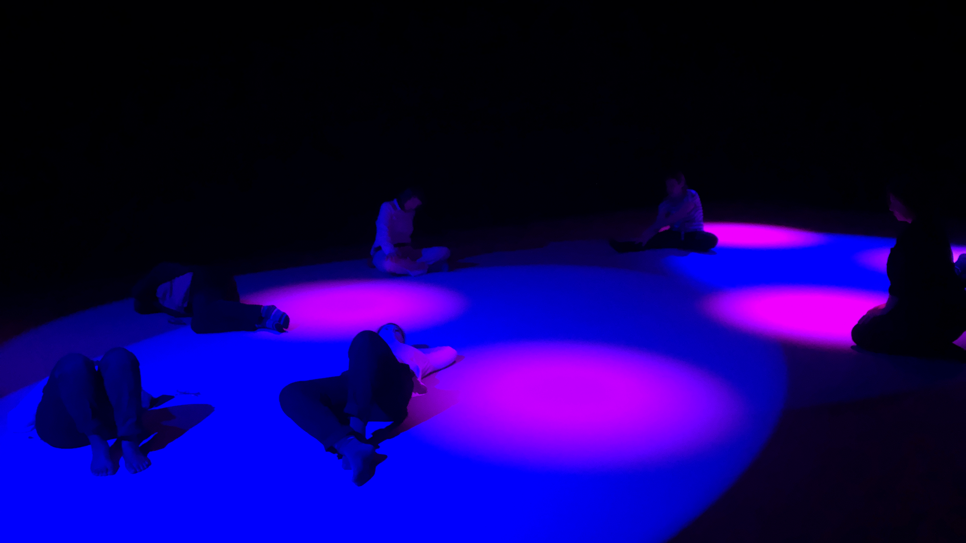 Stillness lab participants lie on the ground immersed in violet light with fuchsia spot lights. 