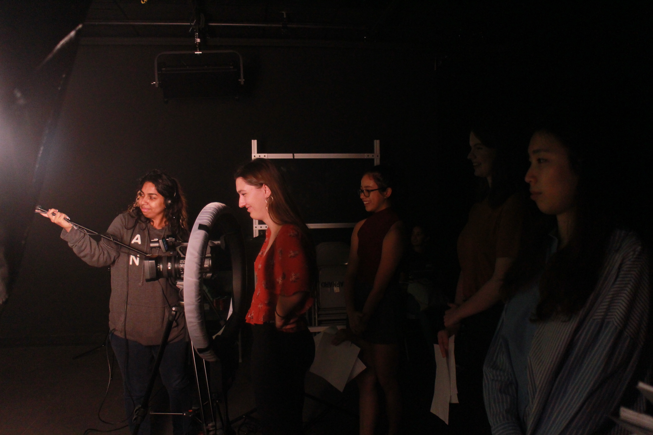 A student extends a microphone boom towards the performers (out of frame), while four other students watch