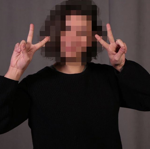 Rebecca makes peace signs with both hands and raises them to their face, which is censored with a mosaic pattern.