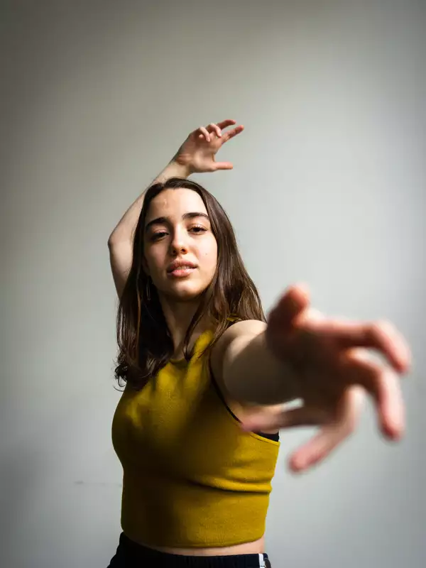 Allison Costa dancing, reaching towards the camera, wearing a yellow shirt