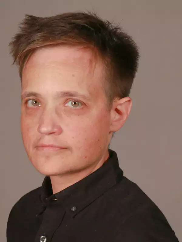 Person with short brown hair wearing a black button-down shift