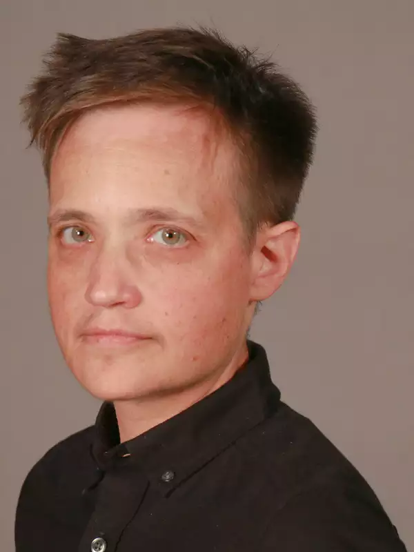 Person with short brown hair wearing a black button-down shift