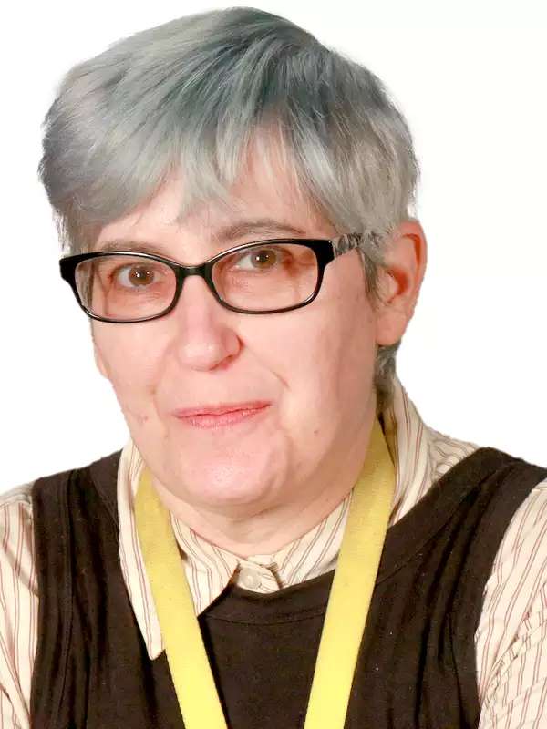 photo of a white woman with light blue hair and glasses, wearing a striped shirt under a tunic